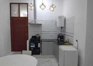 Una cocina compacta con salpicadero blanco de azulejos, una estufa, un fregadero y un refrigerador. Hay luces colgantes sobre la encimera.