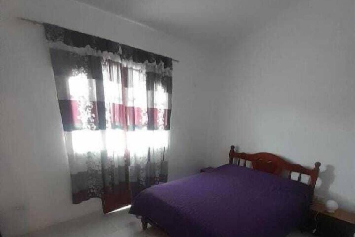 Un dormitorio con cama, cortinas y mesita de noche.