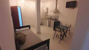 Una habitación pequeña y de concepto abierto con una cama, un escritorio, una silla y un televisor montado en la pared.
