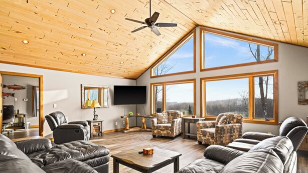 A spacious living room with leather sofas, a ceiling fan, and large windows offering views of the outdoors. - Spacious 5-Bedroom Home with Stunning Views & Privacy, 10 Miles from downtown (Duluth)