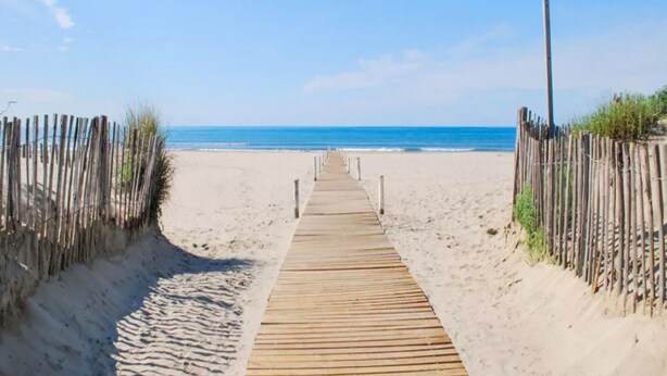 Una passerella di legno conduce a una spiaggia sabbiosa sotto un cielo azzurro limpido.