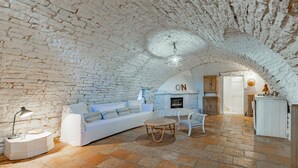 Un interno rustico con pareti in mattoni a vista, un divano bianco, un tavolino rotondo in vimini e una sedia bianca.