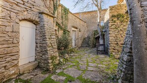 Un cortile in pietra stretto con una porta bianca, un tavolino e una scala che conduce a un livello superiore.