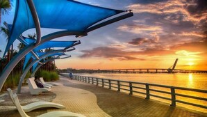 A waterfront promenade with modern sun loungers and a sunset view.