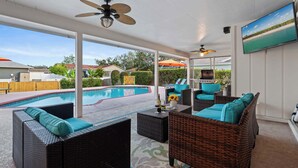 A covered outdoor area with wicker furniture, a pool, and a TV screen displaying a beach scene.