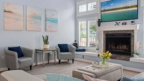 A living room with a fireplace, a large TV, and three beach-themed paintings.