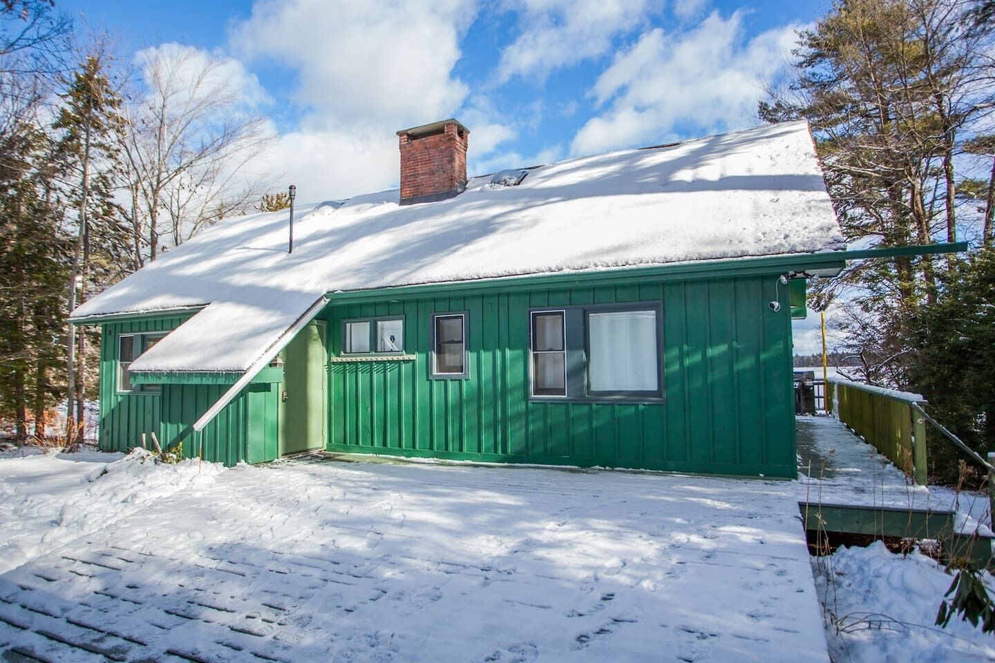 Eine grüne Holzhütte mit schneebedecktem Dach, umgeben von Bäumen.