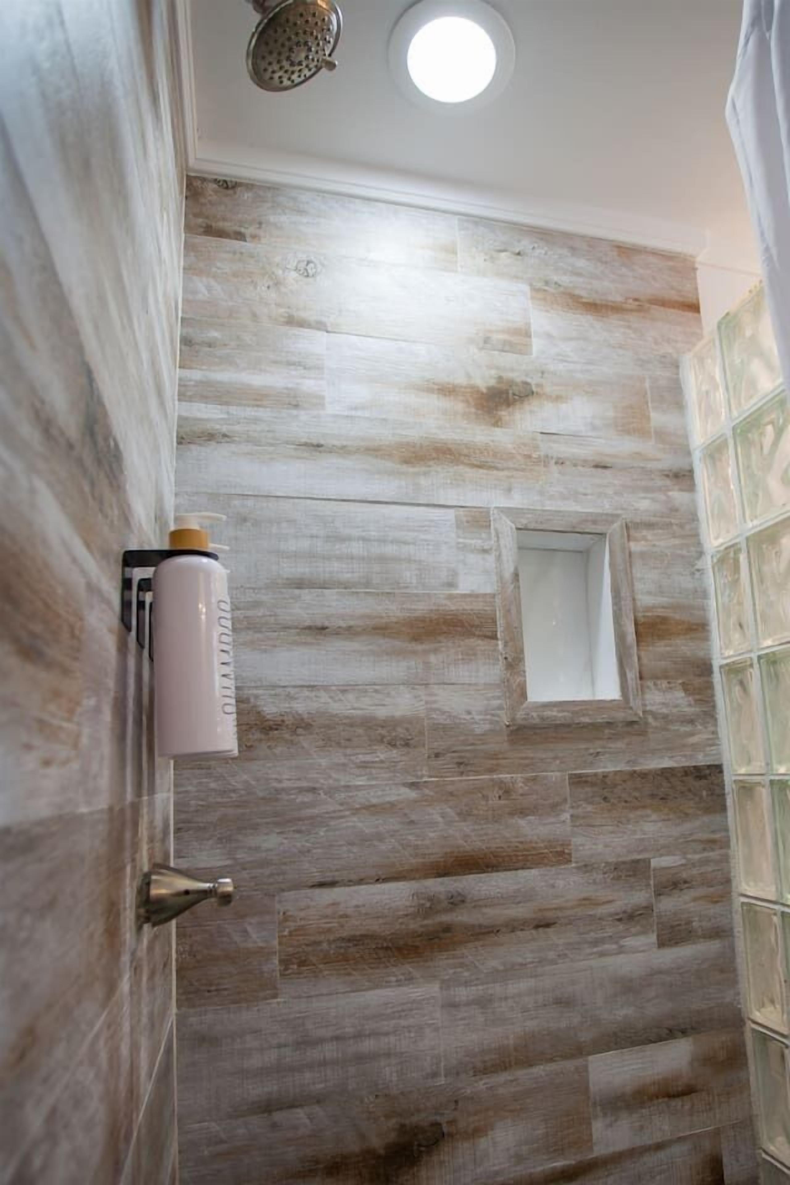 A shower with a wooden wall, a small window, and a showerhead.