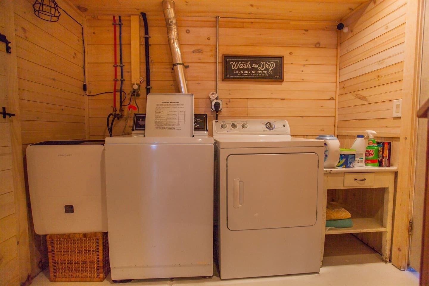 A compact laundry room with a washing machine and dryer, a sign for 'Wash and Dry Laundry Service Co.', and a shelf with cleaning supplies.