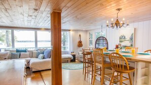 Een gezellig cabin-interieur met een houten eethoek, een bank met decoratieve kussens en een groot raam met uitzicht op een natuurlandschap.