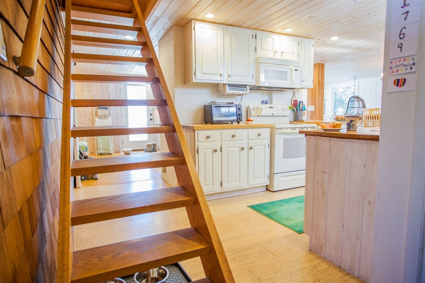 A wooden staircase leading to a kitchen with white cabinets, a microwave, and a stove.