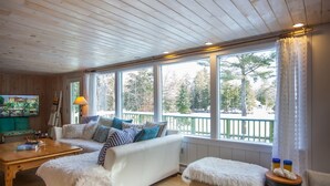 Een knus ingerichte kamer met een witte bank, een houten bijzettafeltje en uitzicht op een besneeuwd terras.