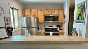 A kitchen with wooden cabinets, stainless steel appliances, and a bar area with two stools.