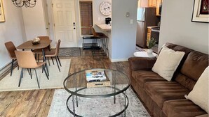 A living room with a brown sofa, a glass coffee table, and a dining area with a wooden table and chairs.