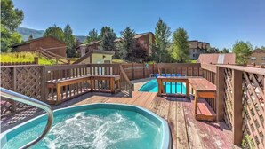 A wooden deck with a hot tub, a pool, and lounge chairs.