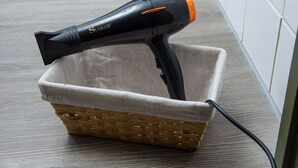 Un secador de pelo negro con punta naranja dentro de una cesta de mimbre sobre un suelo de madera.