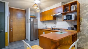 Una cocina compacta con gabinetes de madera, un microondas integrado y una pequeña isla con dos taburetes.
