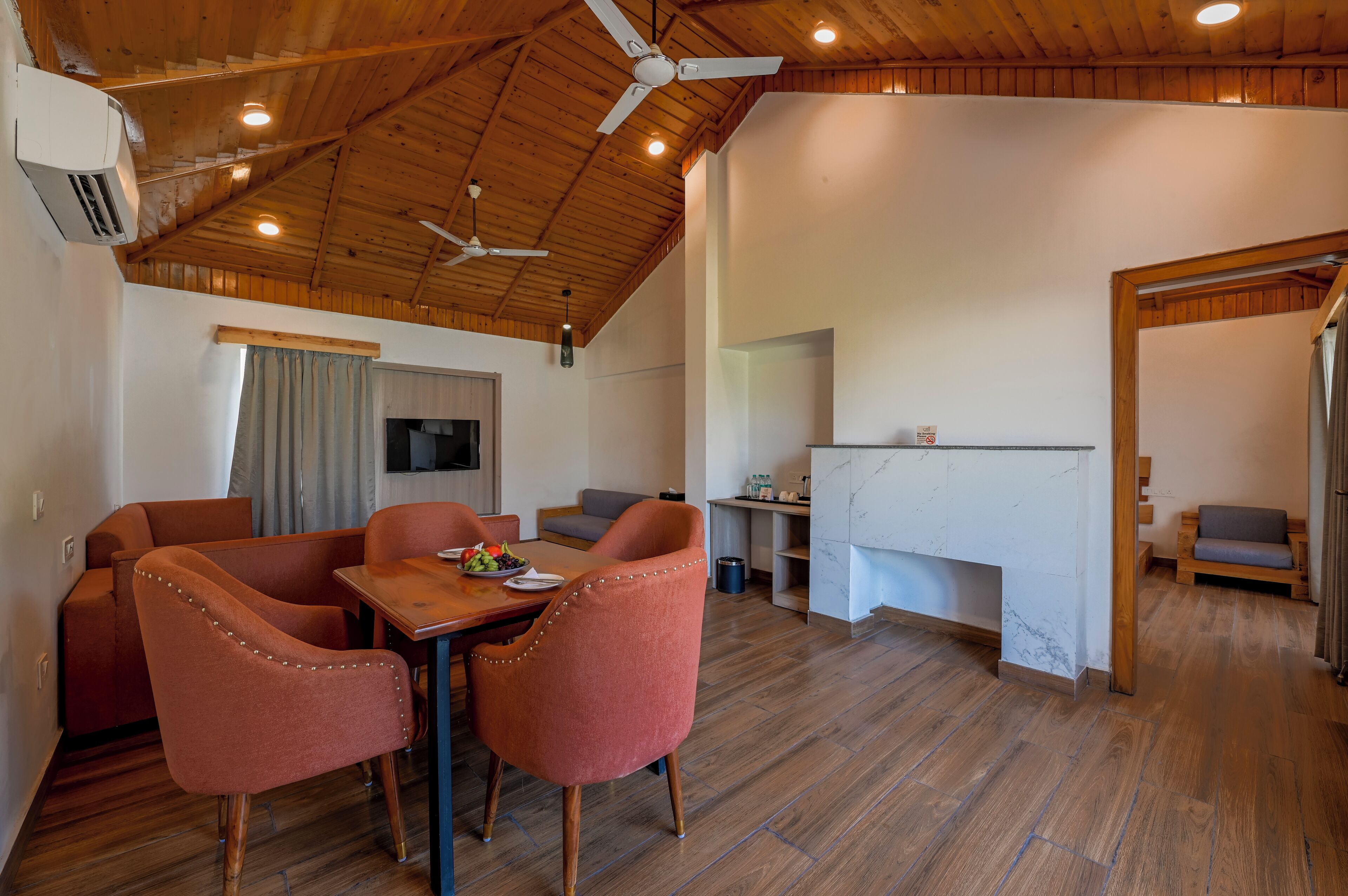 A spacious room with a wooden ceiling, a dining area with two chairs and a table, a kitchen area, and a seating area with a couch.