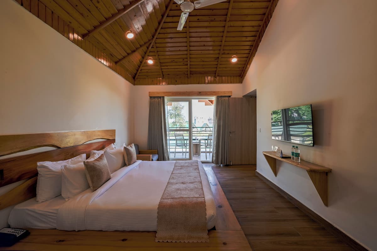 A bedroom with a wooden ceiling, a large bed with white linens, a TV on the wall, and a balcony with curtains.