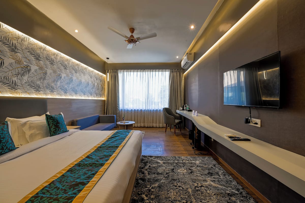 A modern hotel room with a large bed, a desk, a chair, a TV, and a ceiling fan.