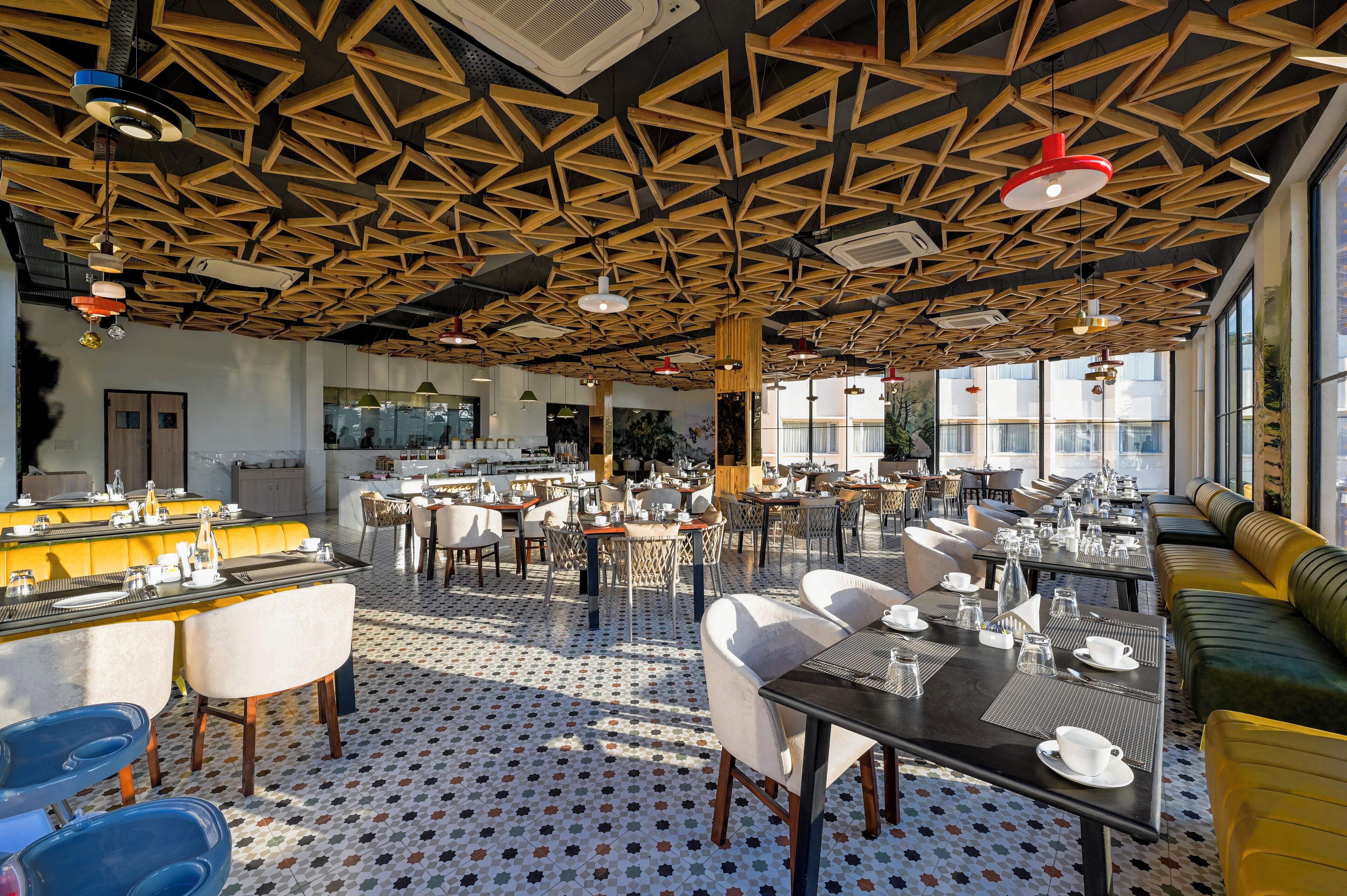 Un restaurante espacioso con techo de madera con diseño geométrico, varias zonas de comedor y suelo estampado.