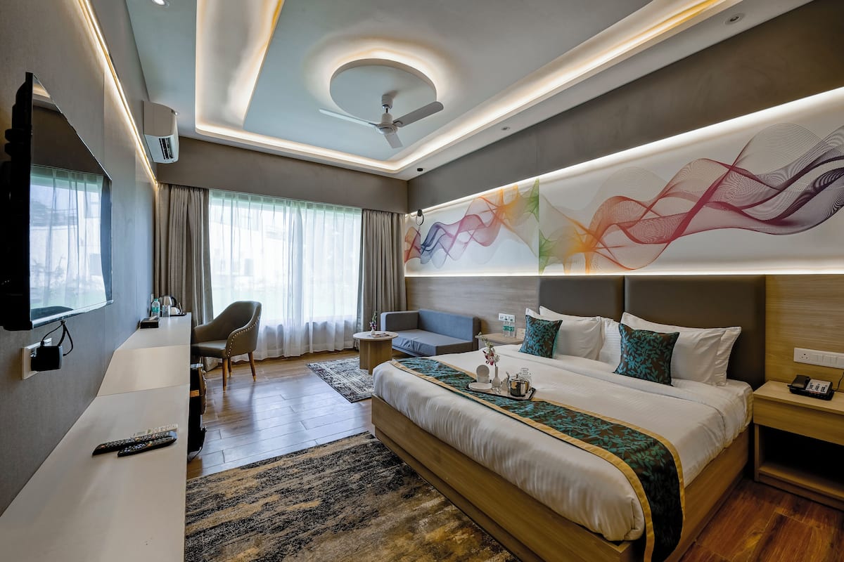 A modern hotel room with a large bed, a desk, a chair, and a ceiling fan.