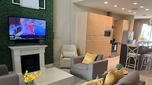 Una sala de estar moderna con televisor de pantalla plana, chimenea y una zona de cocina con armarios de madera y comedor.