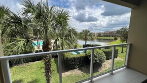 Un balcón con vista a una piscina, palmeras y un edificio al fondo.