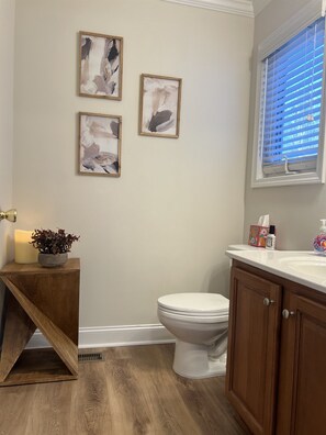 Ein Badezimmer mit Toilette, Holzwaschtisch und drei abstrakten Bildern an der Wand.