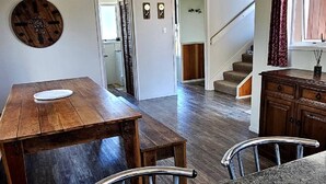 A spacious living area with a wooden dining table, a kitchen counter, and a staircase leading to another level.