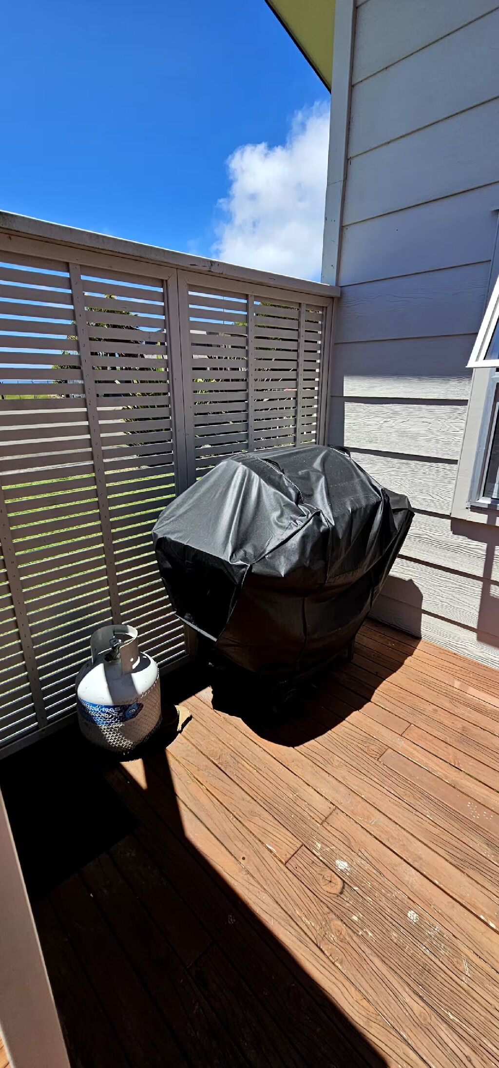 A covered grill on a wooden deck with a metal fence and a gas cylinder nearby.
