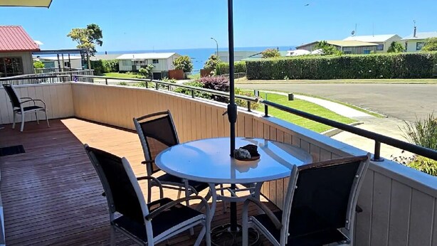 A wooden deck with a round table and chairs, an umbrella, and a view of the ocean and buildings.