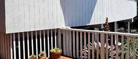 Une terrasse en bois agrémentée de plantes en pot, d’un grand parasol et d’un bâtiment blanc doté d’un balcon.
