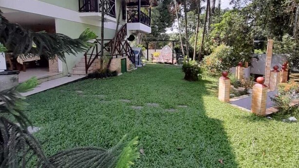 A courtyard with a well-maintained lawn, palm trees, and a building with a balcony. - House in Guapimirim/Caneca Fina - Gated community (Guapimirim)