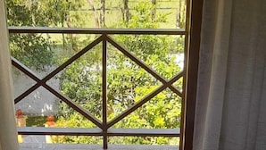 A bedroom with a bed, a blue towel, and a white towel. There is a window with a view of greenery outside. - House in Guapimirim/Caneca Fina - Gated community (Guapimirim)