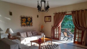 A living room with a sofa, a coffee table, a lamp, a chandelier, a patterned rug, and a balcony with curtains. - House in Guapimirim/Caneca Fina - Gated community (Guapimirim)