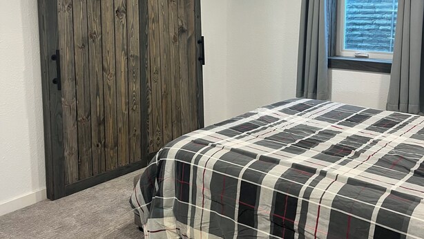 A bedroom with a large bed, a wardrobe, and a window with curtains. - Rally Rental:  4-bedroom house - walking distance from Sturgis Main Street. (Sturgis)