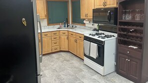 A kitchen with wooden cabinets, a stove, a microwave, and a wine rack. - Rally Rental:  4-bedroom house - walking distance from Sturgis Main Street. (Sturgis)