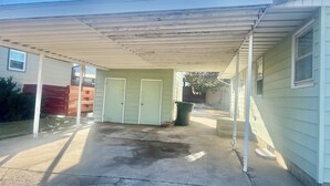 A covered patio area with a concrete floor, two doors, and a small trash bin. - Rally Rental:  4-bedroom house - walking distance from Sturgis Main Street. (Sturgis)