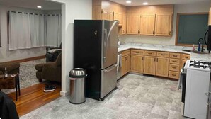 A compact kitchen with wooden cabinets, a stainless steel refrigerator, a gas stove, and a trash can. - Rally Rental:  4-bedroom house - walking distance from Sturgis Main Street. (Sturgis)