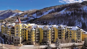 Un hotel de varios pisos con fachada amarilla, situado en una zona montañosa con laderas cubiertas de nieve.