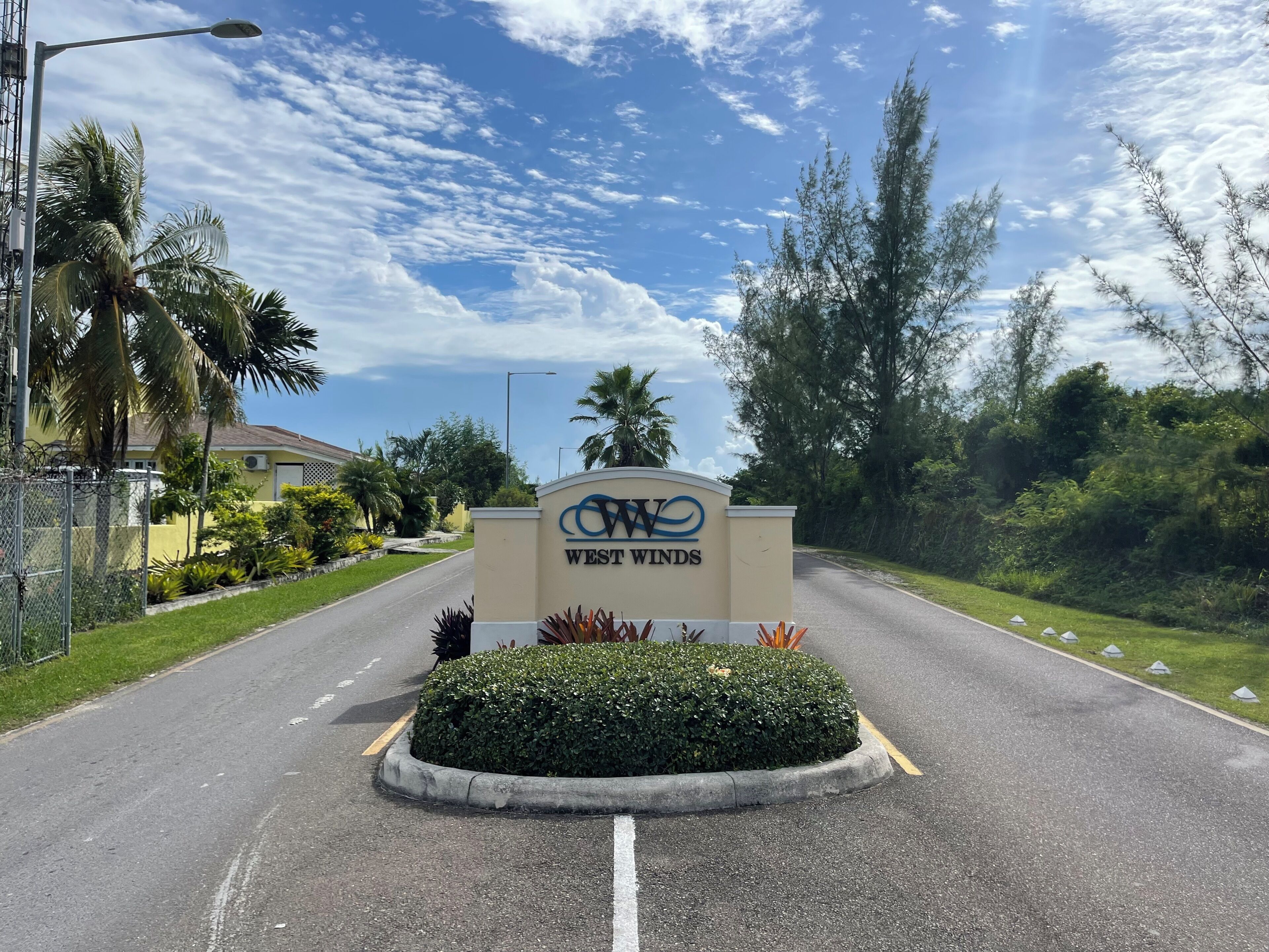 A road sign for West Winds with a clear sky and palm trees in the background.