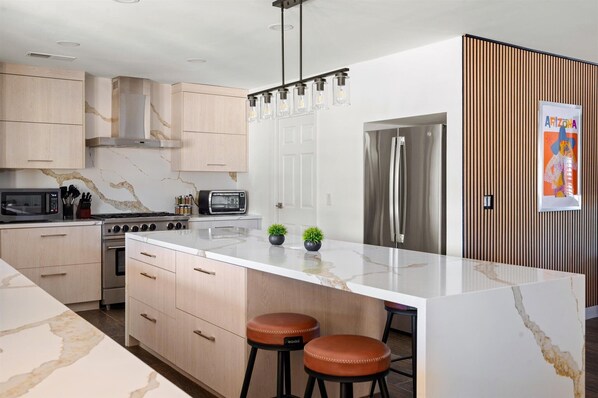 A modern kitchen with a large island, stainless steel appliances, and wooden cabinetry.
