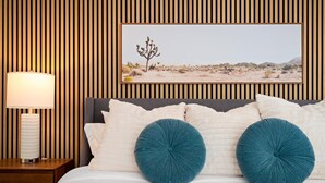 A bedroom with a wooden slat wall, a framed desert landscape picture, a bedside lamp, and two teal pillows on the bed. - Scottsdale Retreat | Pool & Spa | GameRoom (Scottsdale)