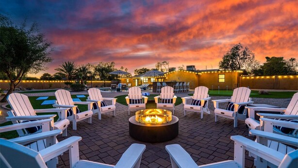 A patio area with Adirondack chairs arranged around a central fire pit, under a sunset sky. - Scottsdale Retreat | Pool & Spa | GameRoom (Scottsdale)