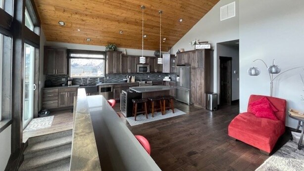 A spacious kitchen with a central island, dark wooden flooring, and a high wooden ceiling.
