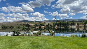 A grassy field with a lake, houses, and mountains in the background.