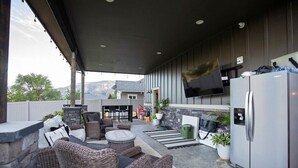 An outdoor patio with wicker furniture, a stone wall, a flat-screen TV, and a refrigerator.