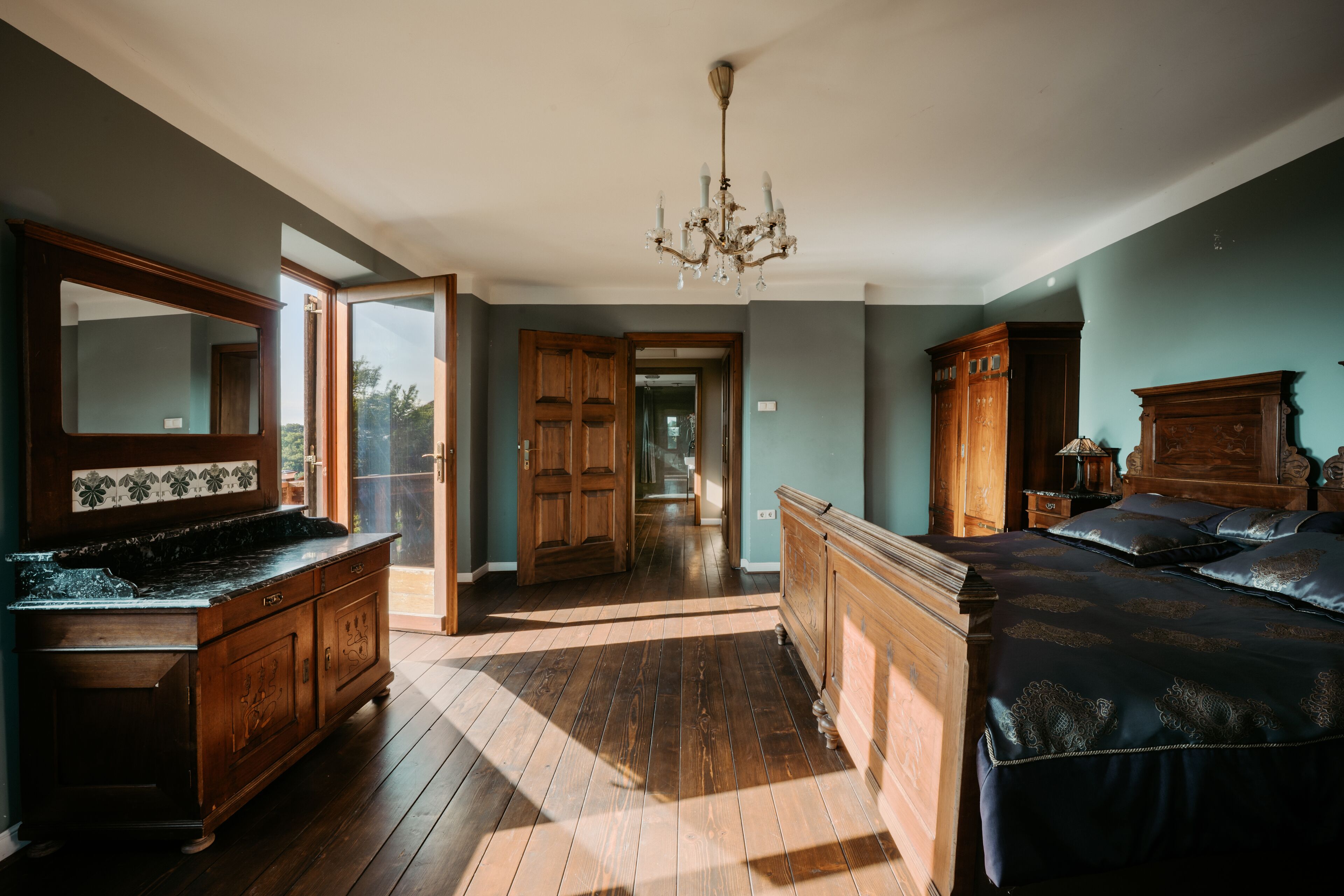 Een ruime slaapkamer met een groot bed, een houten garderobe en een spiegel boven de dressoir.