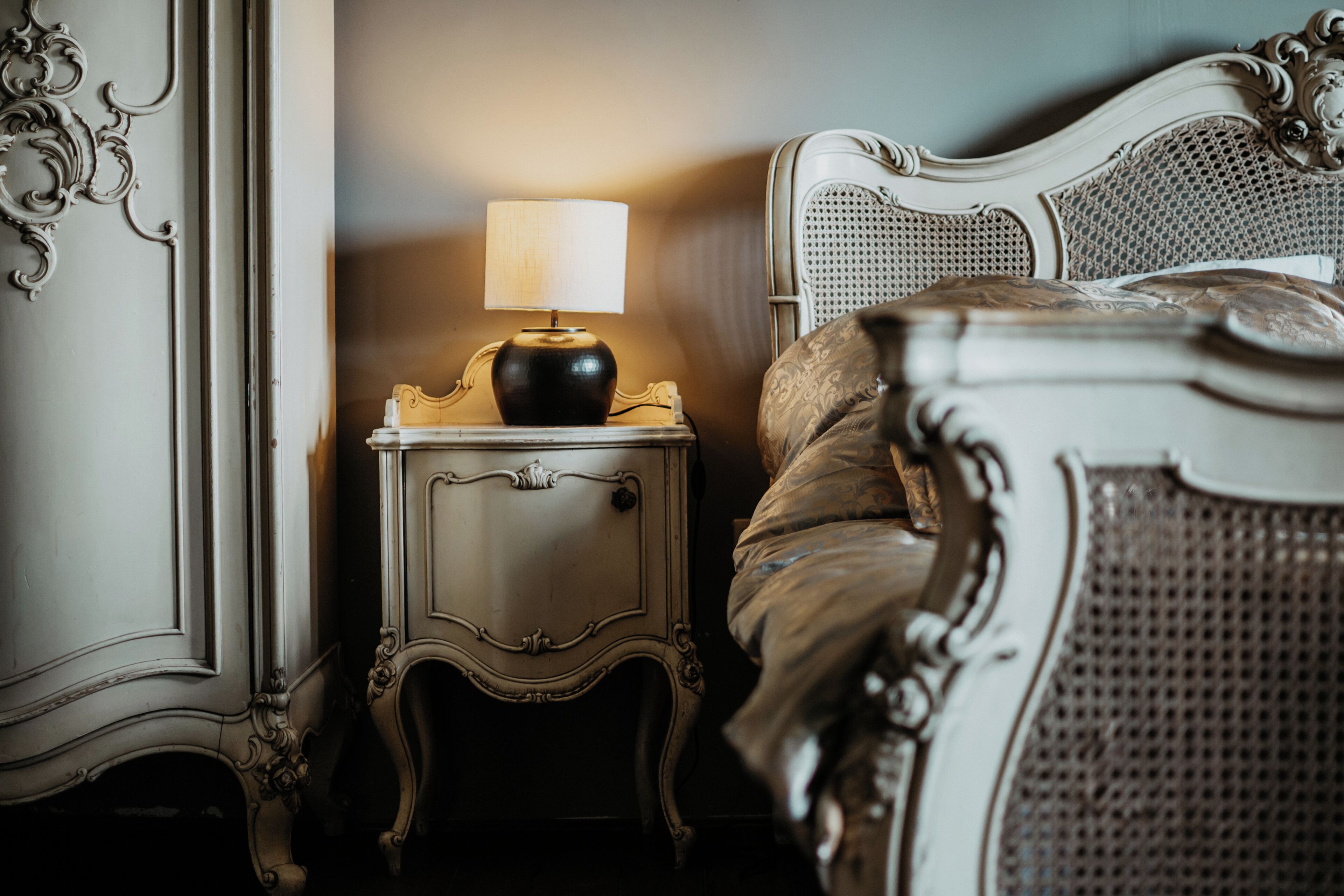 Una camera da letto con un letto classico, un comodino decorato e una lampada.